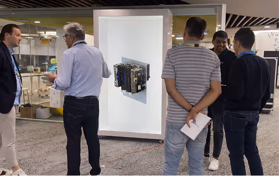 Five men standing and conversing in a modern office space with a transparent display featuring computer hardware mounted on a lit panel.