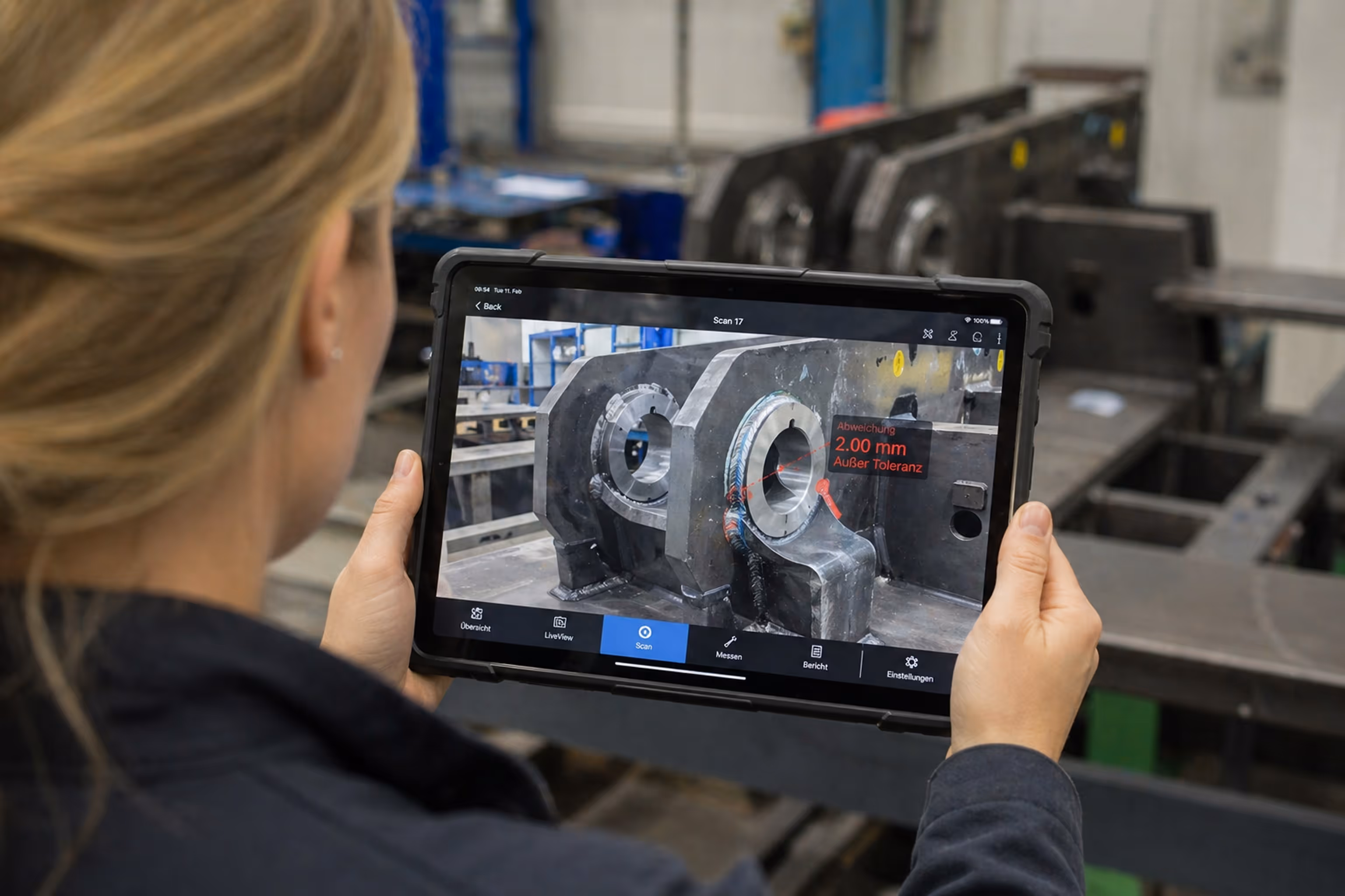 Person holding a tablet displaying a 3D scan of metal parts with measurement details in a workshop setting.