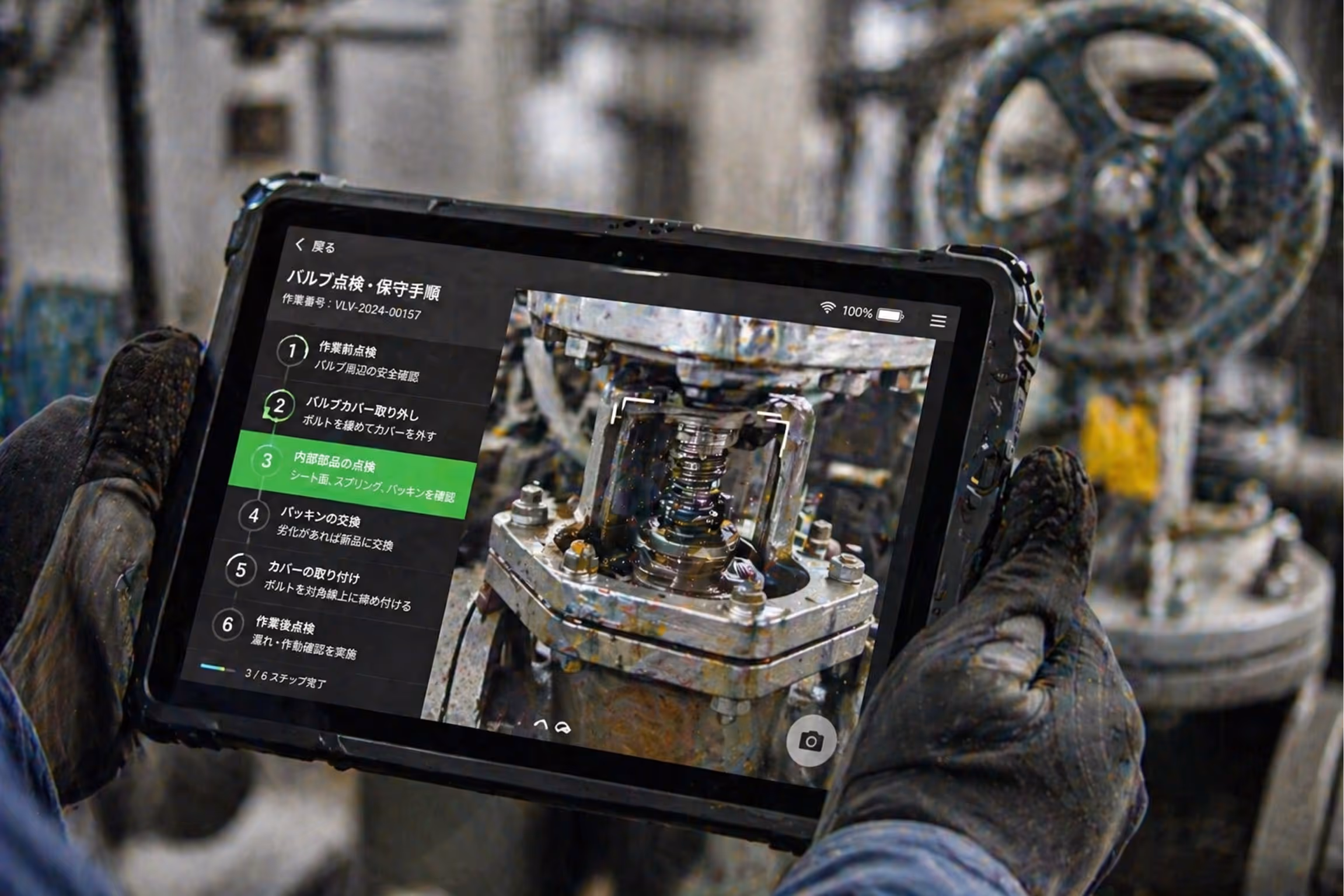 Gloved hands holding a rugged tablet showing detailed Japanese instructions for valve inspection and maintenance, with a close-up image of a valve component on screen.