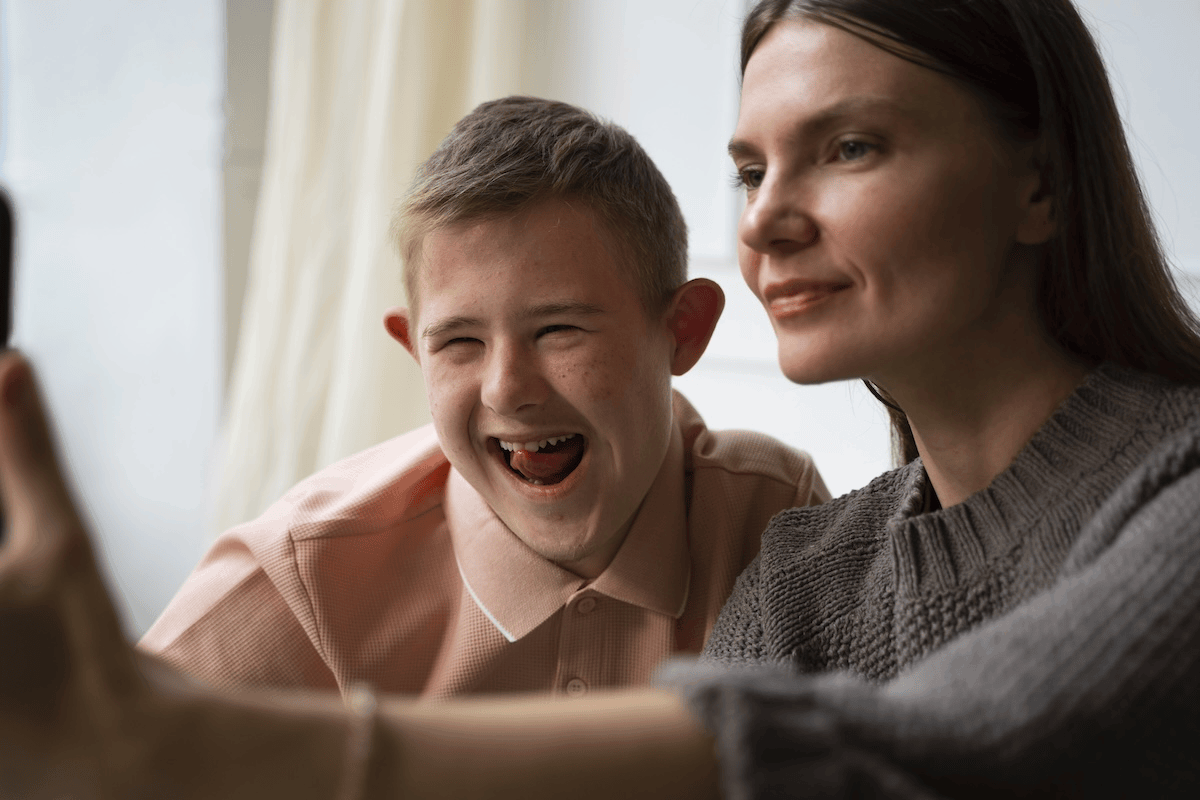 Smiling grandmother and grandson taking a close-up selfie indoors, both looking at the camera.