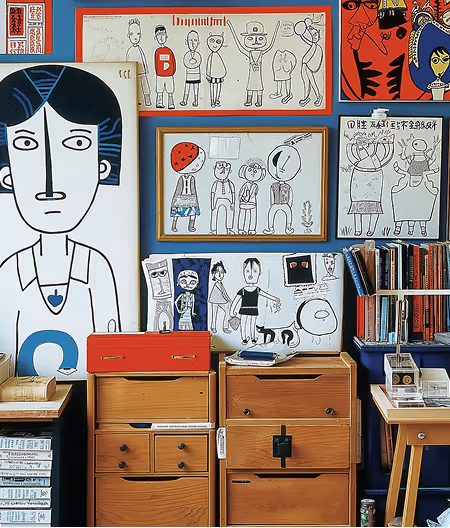 Room corner with wooden drawers and shelves, adorned with eclectic framed black-and-white and colorful cartoon-style artwork on a dark blue wall.