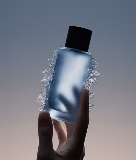 Hand holding a frosted glass bottle with a black cap surrounded by splashing water against a gradient background.