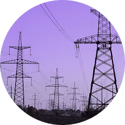 Multiple electricity transmission towers with power lines against a purple evening sky.
