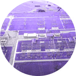 Aerial view of an electrical substation with transformers and power lines in a fenced area.