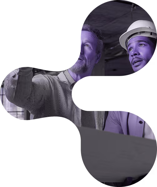 Two men, one in a hard hat, discuss plans in an unfinished industrial building.