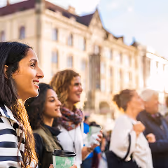 Group of diverse people standing outdoors in sunlight, smiling and holding drinks.