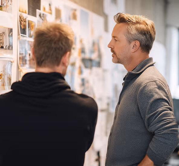 Two men discussing and reviewing images and notes pinned on a wall in a collaborative workspace.