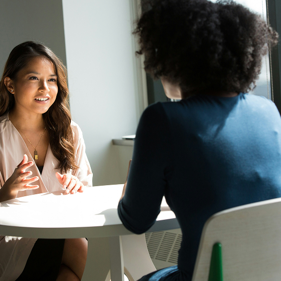 Two women sitting at a table engaged in a friendly conversation in a well-lit room.