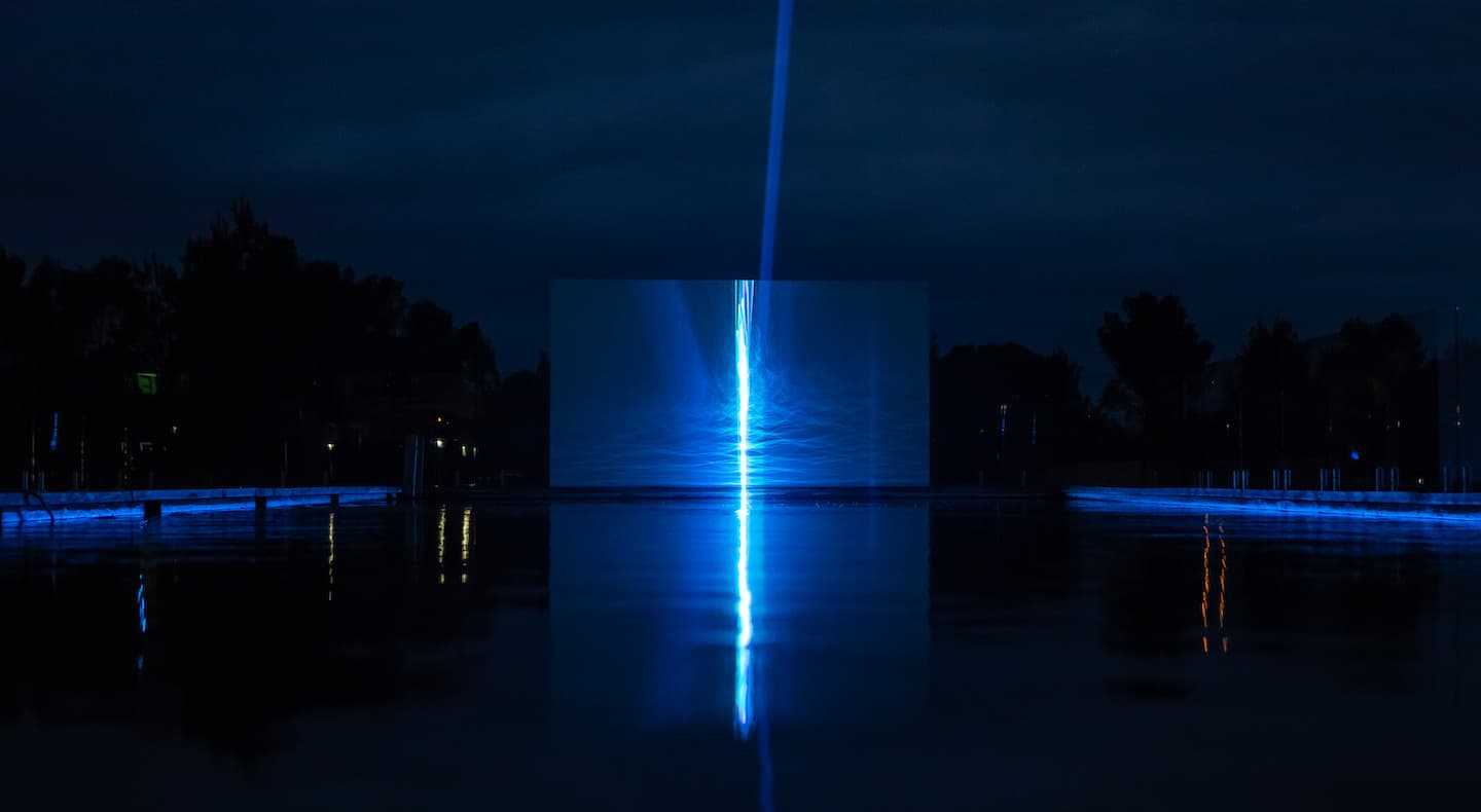 Modern glass structure with orange neon lighting lines in an urban plaza during dusk.