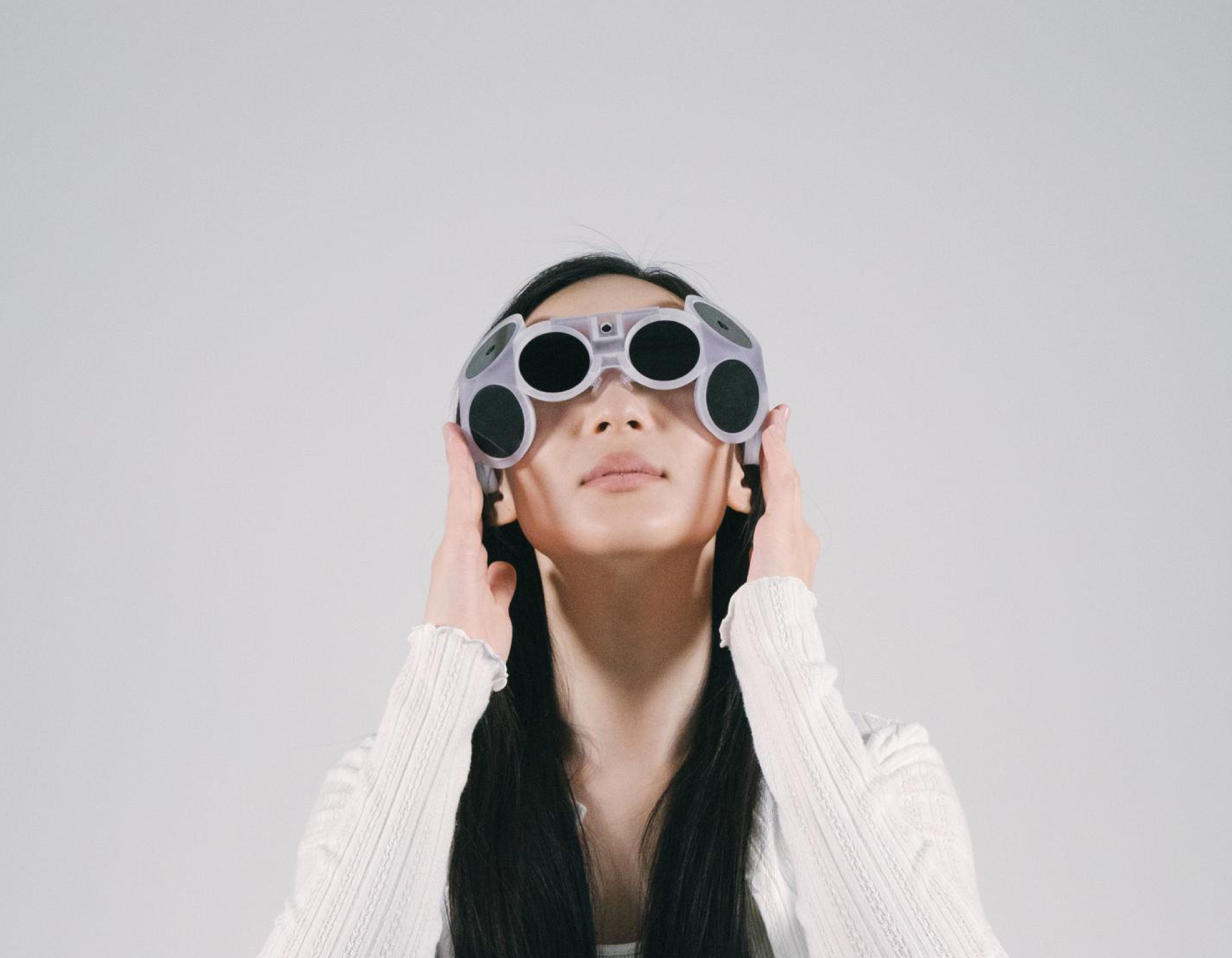 Femme portant un casque futuriste gris avec plusieurs capteurs circulaires noirs sur les yeux.