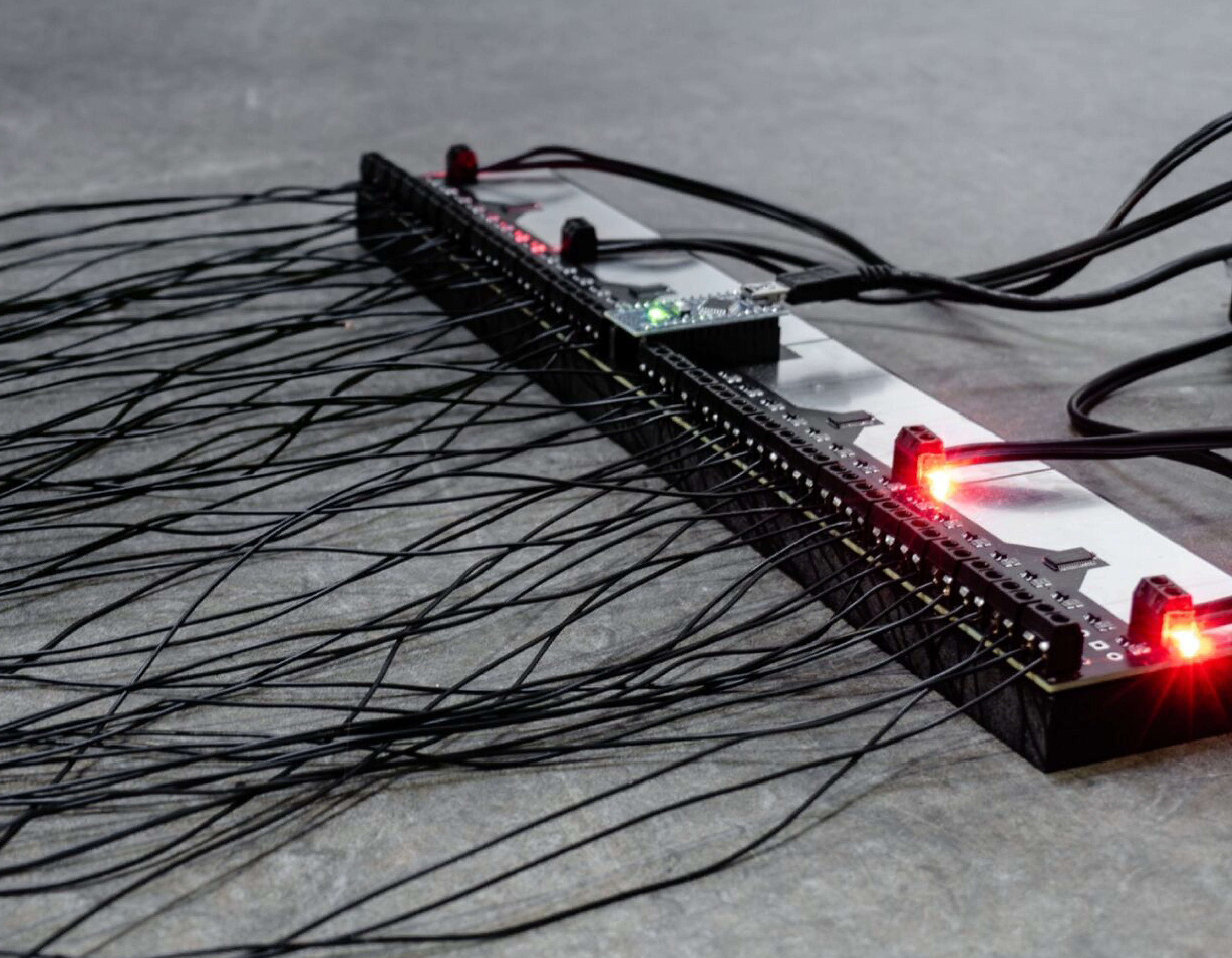Module électronique avec multiples câbles noirs connectés, posé sur une surface grise.