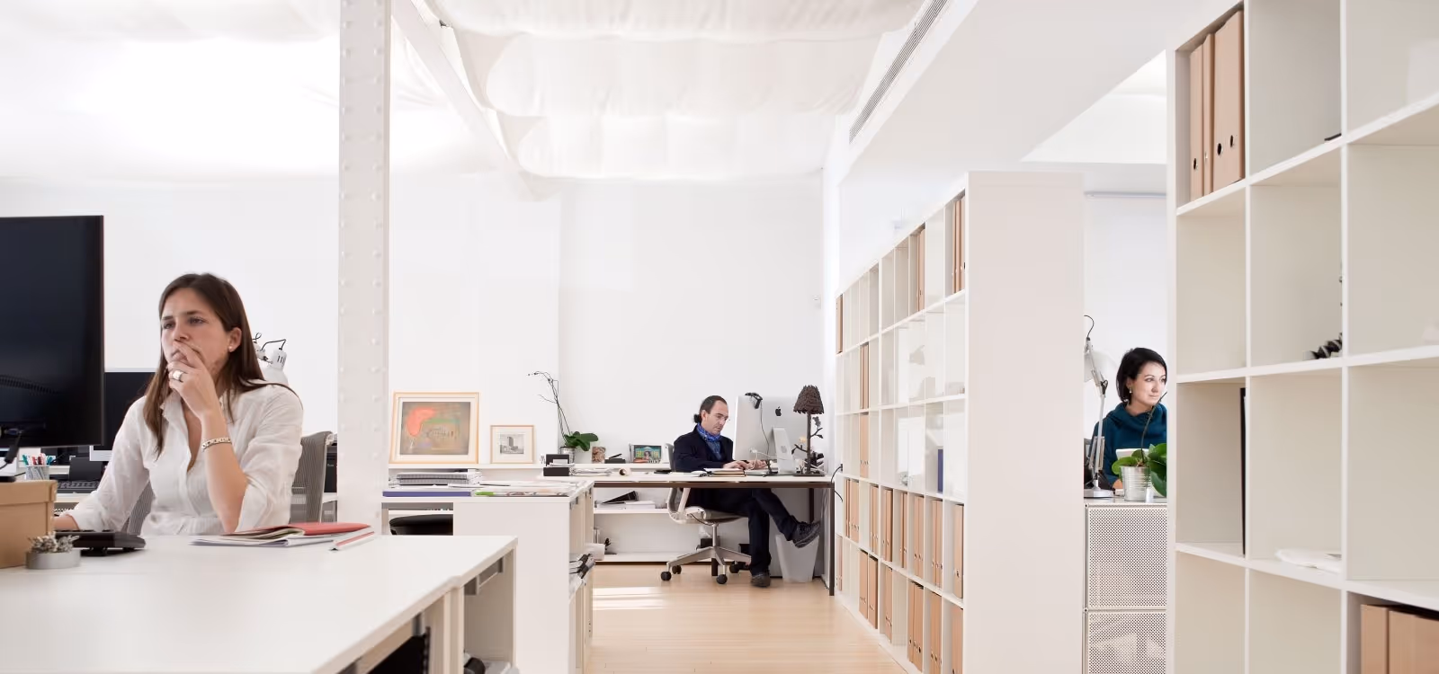 Open-plan architecture office with three team members working at desks.
