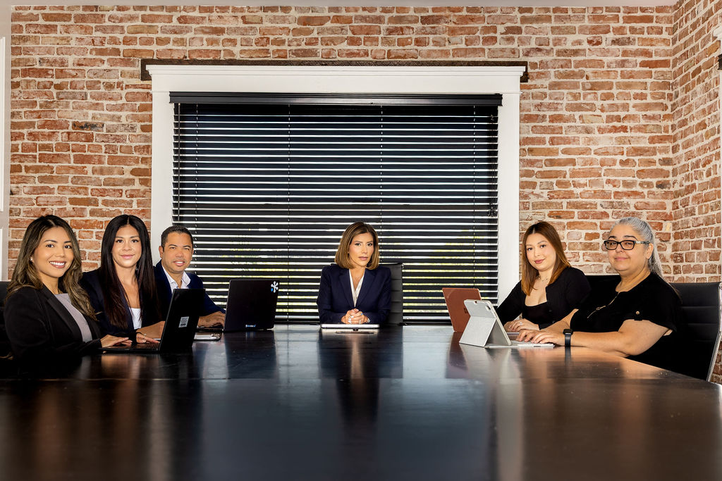 Esli Frias sitting on the edge of a conference table with four other people in a brick-walled meeting room, two working on laptops.