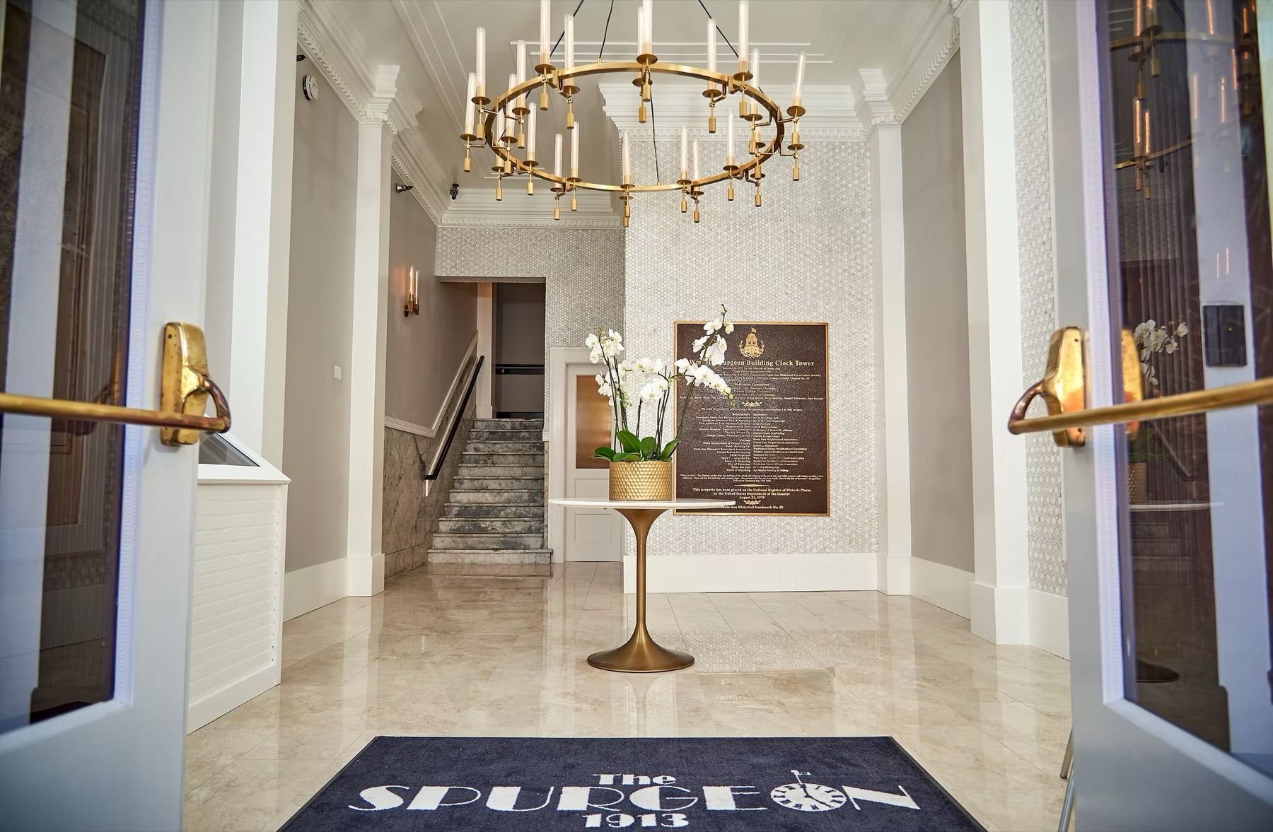 The lobby of the Spurgeon Building: marble floor, a brass chandelier, and the National Register of Historic Places plaque beside the stairs. The mat reads "The Spurgeon 1913".