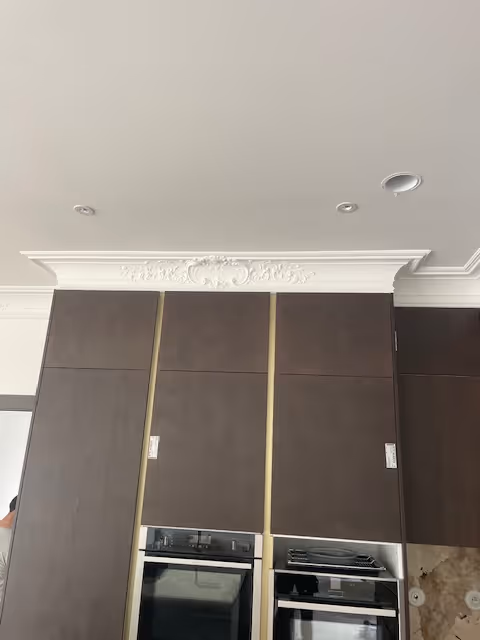 Dark brown kitchen cabinets with built-in oven and intricate white decorative ceiling molding above.