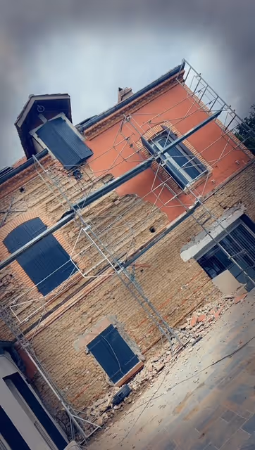 Old brick and plaster building under repair with metal scaffolding and closed dark shutters on windows.