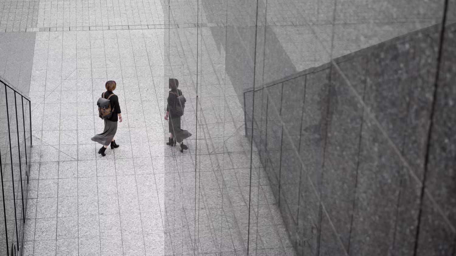 Business professional walking beside a modern glass building with reflection