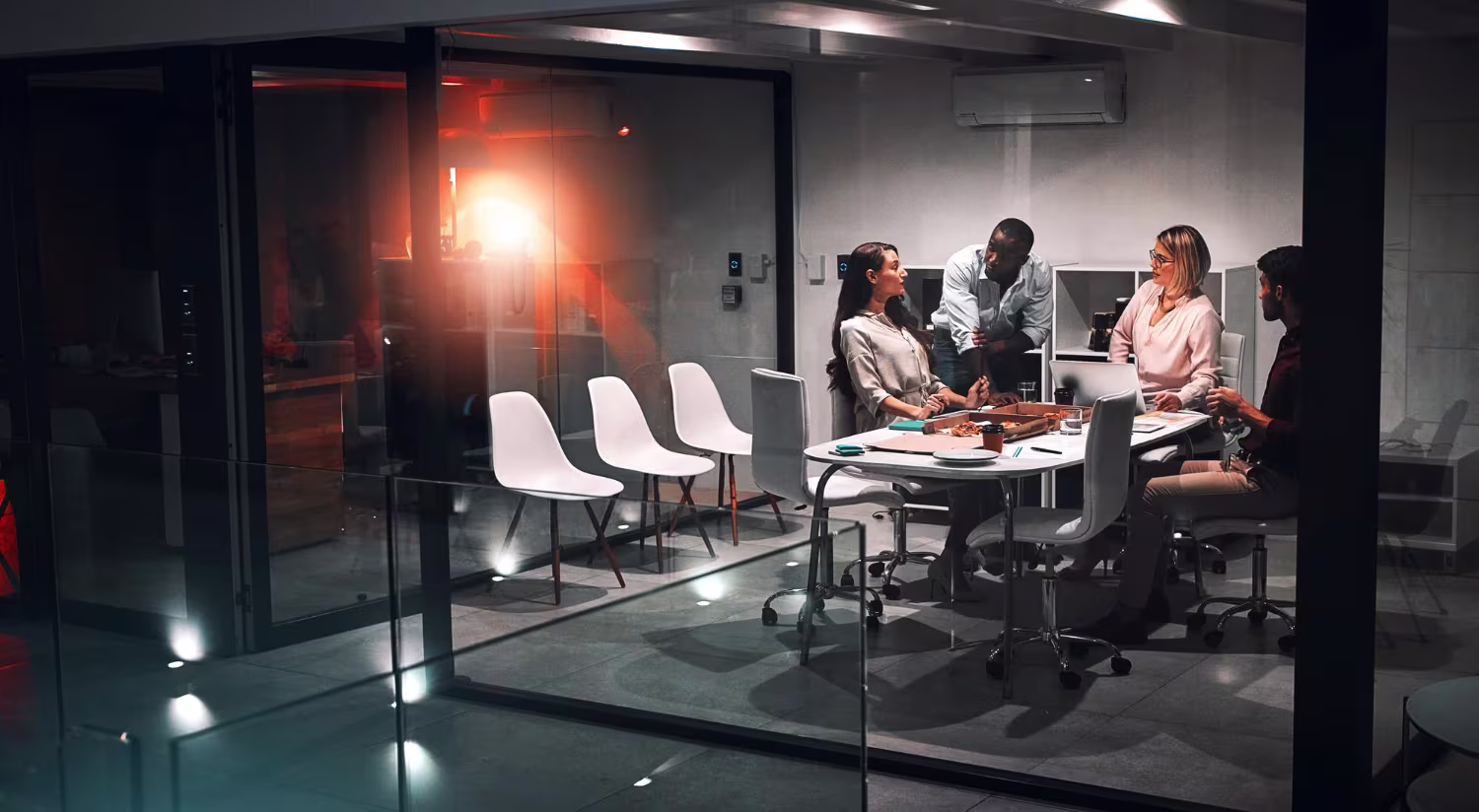Business team in a focused strategy meeting inside a glass office at night
