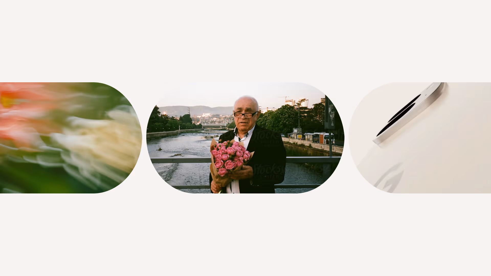 Elderly man wearing glasses holding a bouquet of pink roses standing on a bridge over a river with trees and buildings in the background.