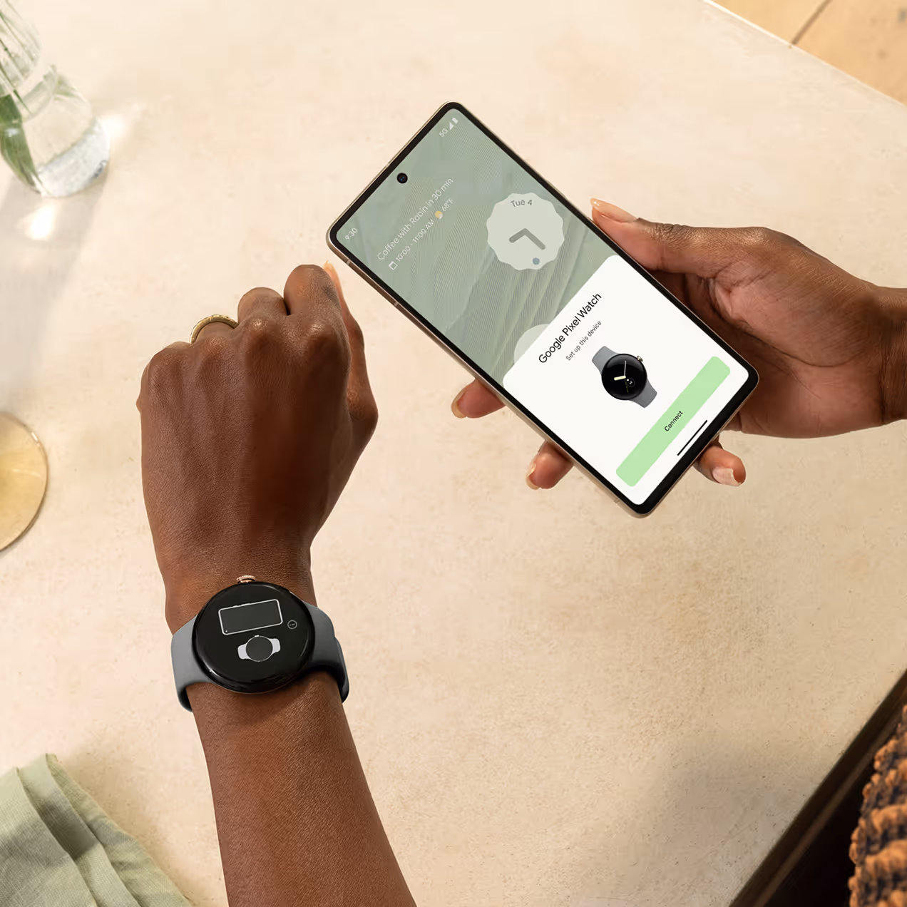 Person wearing a Google Pixel Watch showing a low battery icon while holding a phone displaying the Pixel Watch setup screen.