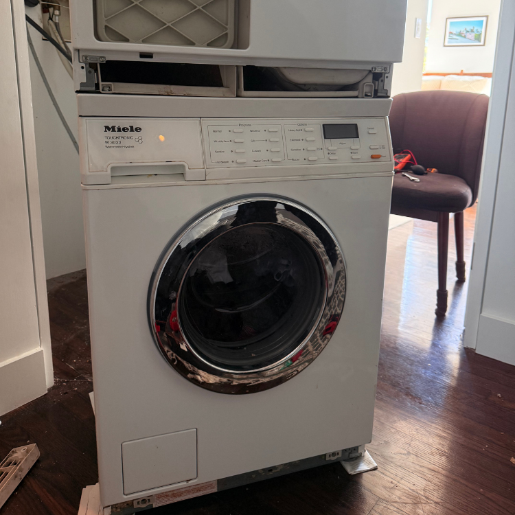 White Miele front-loading washing machine with control panel and circular door in a home setting.