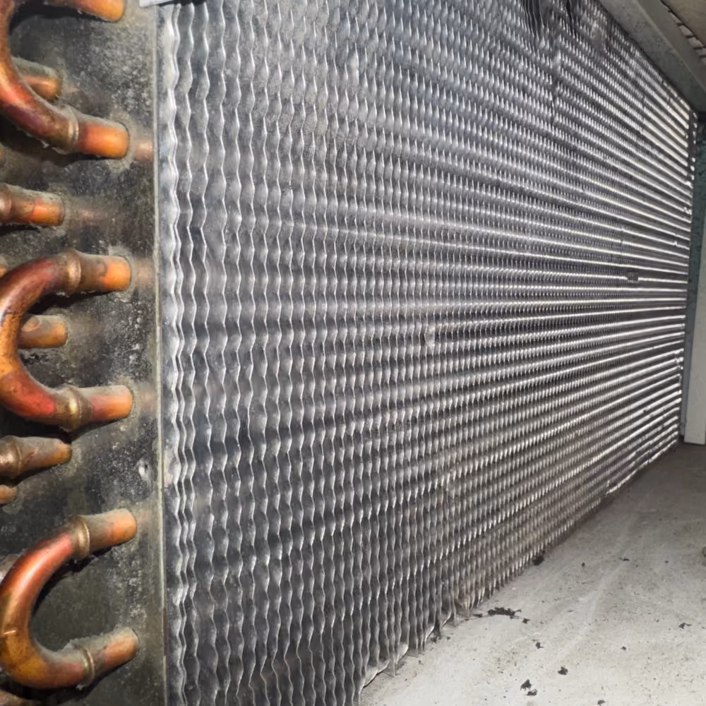 Close-up of a metal air handler coil with copper pipes on the side inside a unit.