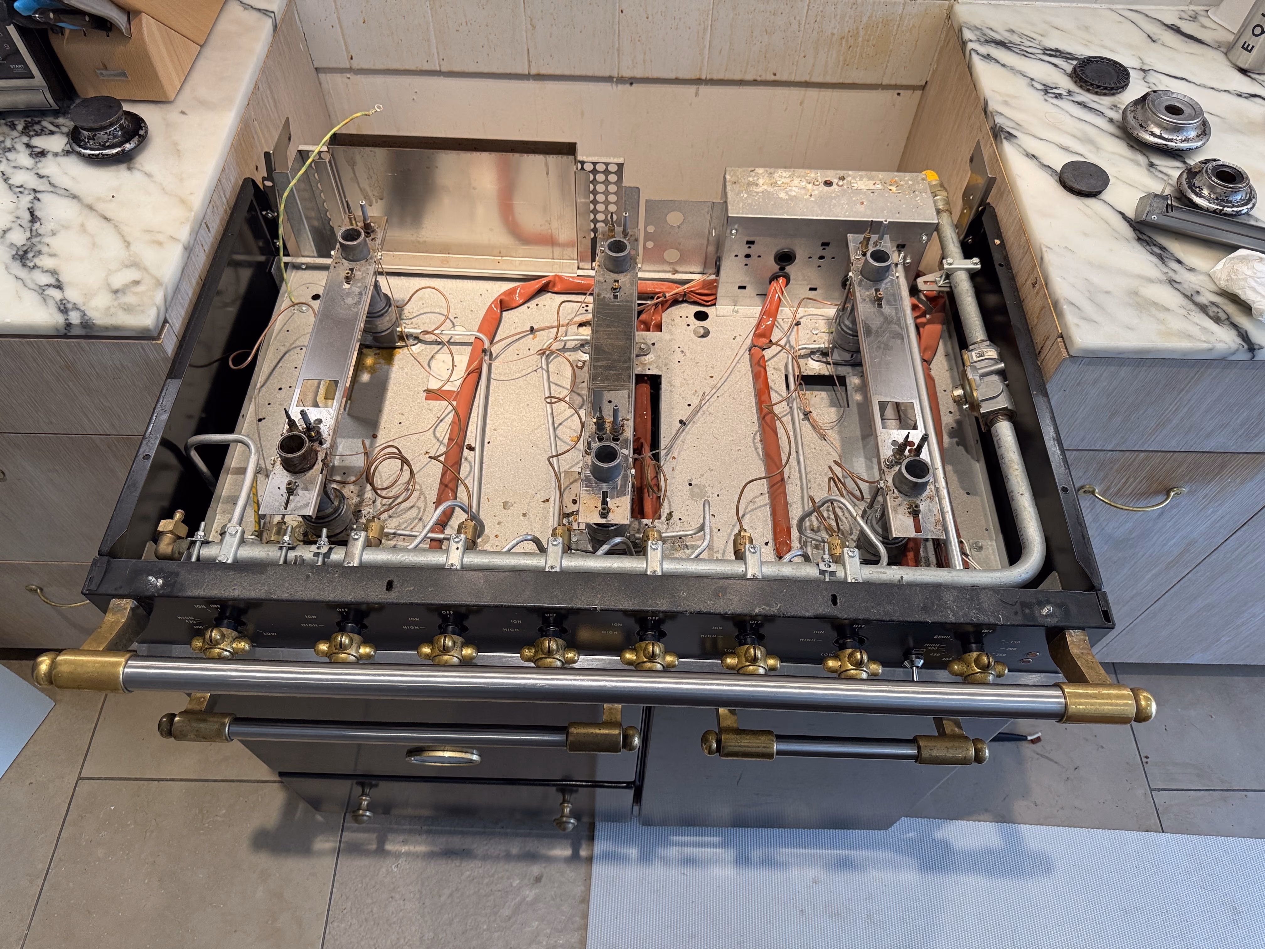 Gas cooktop with its burners and grates removed, showing gas pipes and wiring inside.
