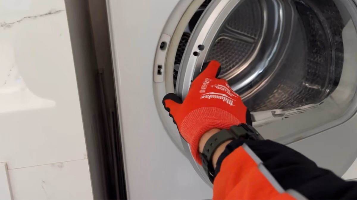 Gloved hand pointing toward the inside of an open dryer drum.