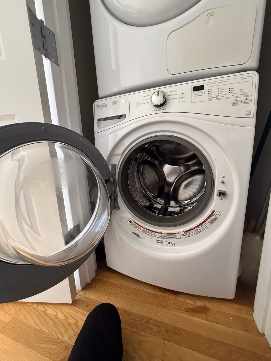 Whirlpool front-load washer beneath a stacked dryer, with the washer door open during the service visit