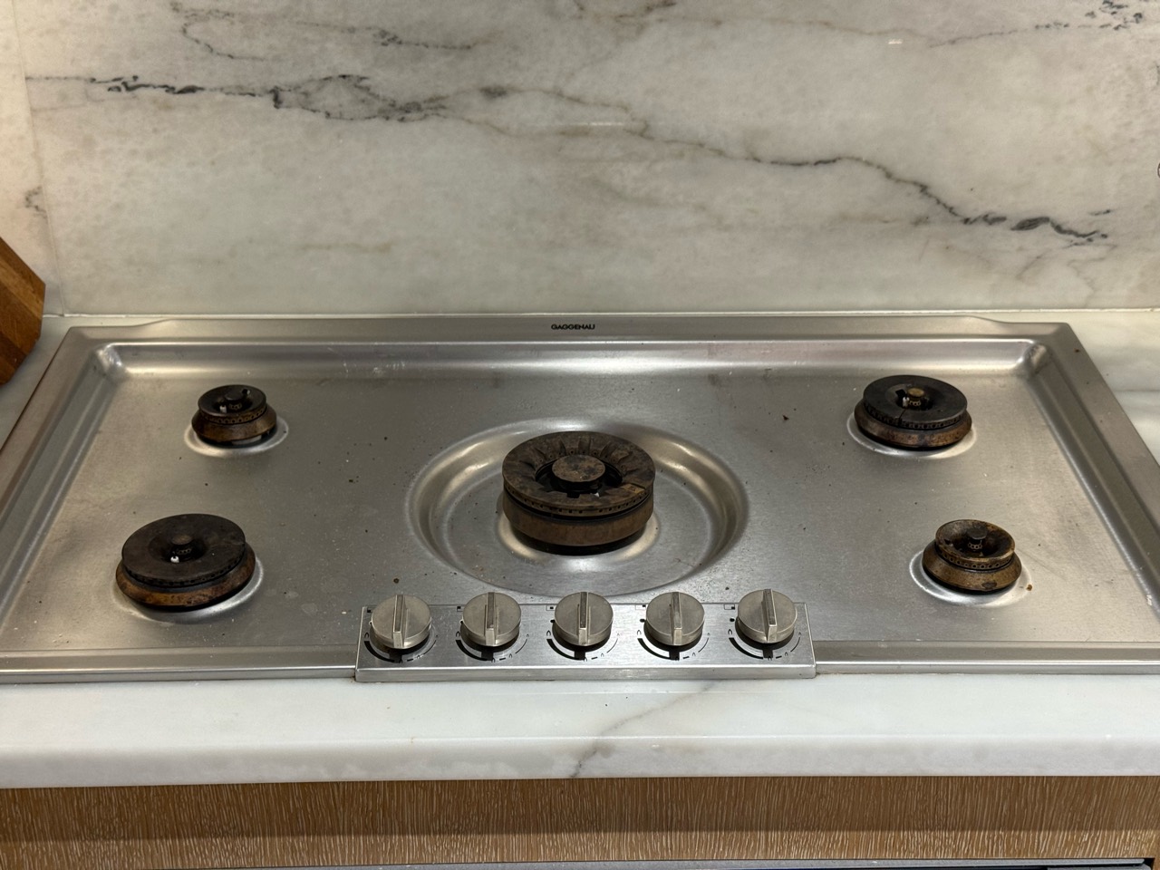The same five-burner Gaggenau cooktop before restoration, with visibly darkened burner components