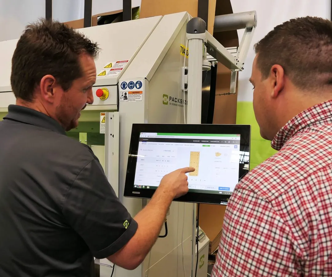 Ein Foto von zwei Mitarbeitern, die die Touchscreen-Oberfläche einer Packsize-Maschine benutzen.
