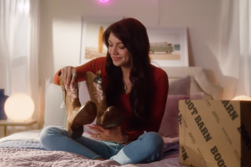 A photo of a woman opening a right-sized package containing a pair of boots.