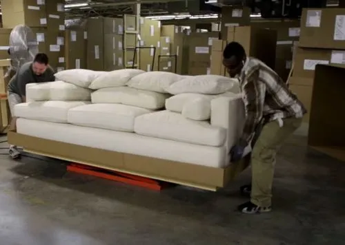 A photo of two Ej Victor employees packaging a sofa in a custom-printed box produced on a Packsize machine.