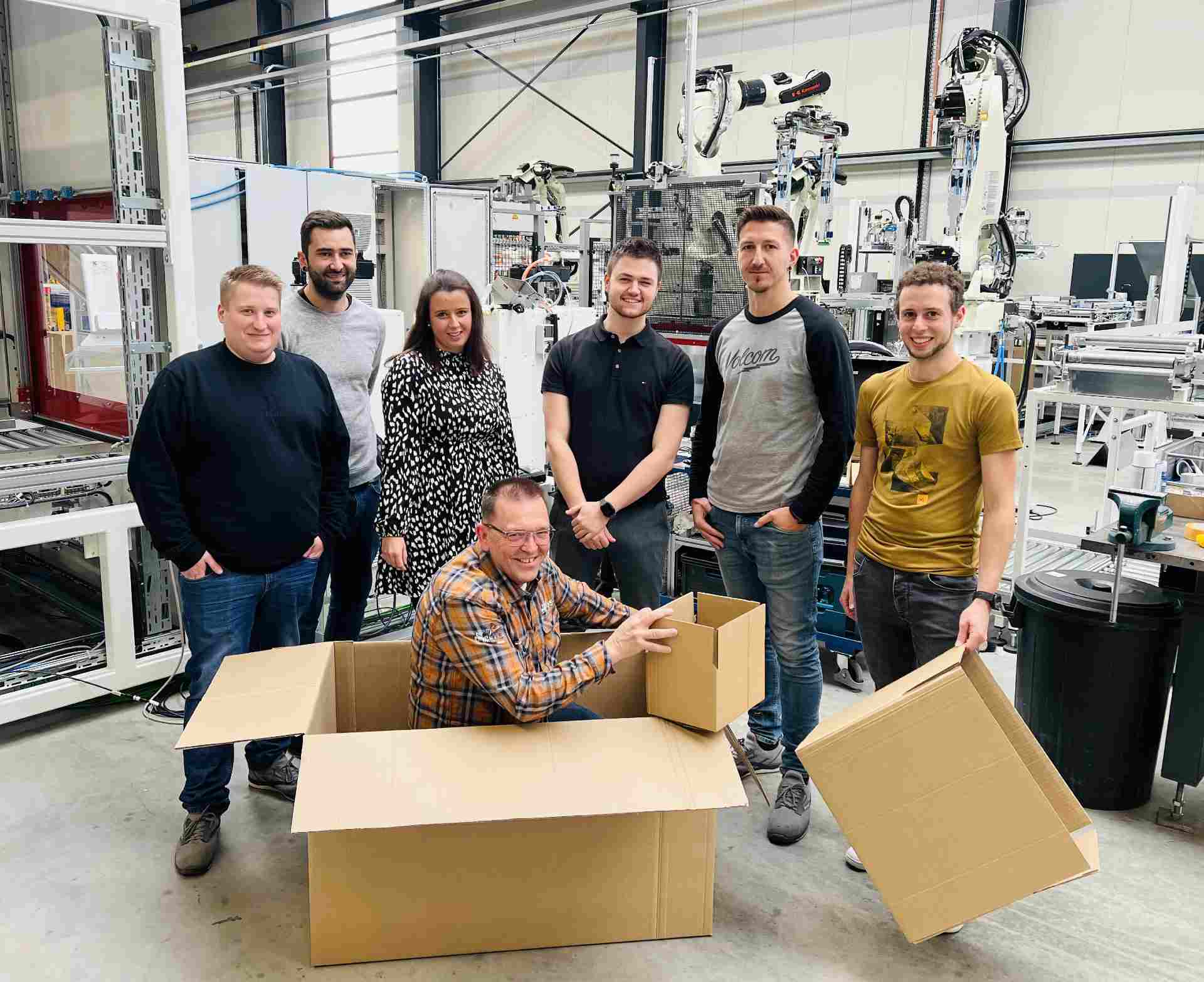 The VEGA team in front of its outer packaging solution with pick-and-pack robots in the background (+ smallest and biggest possible box).