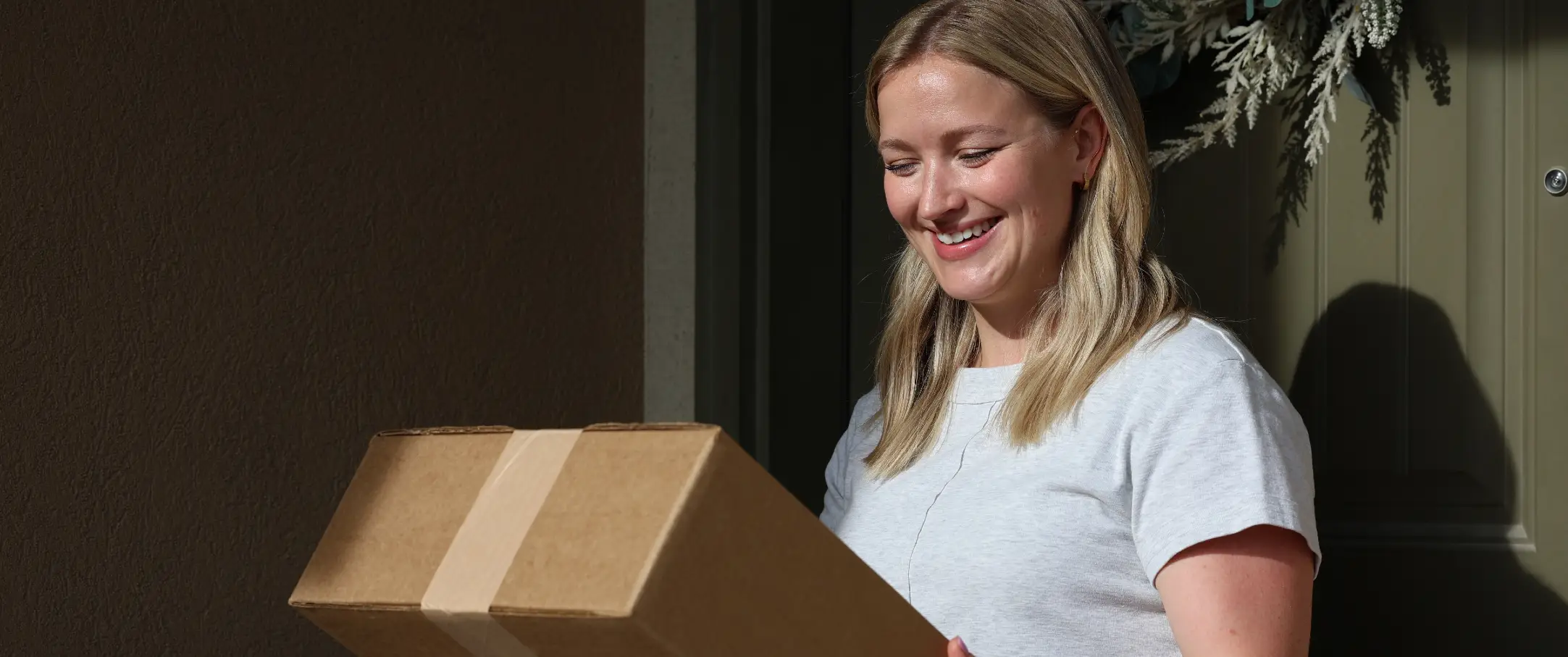 Zadowolona kobieta odbiera przed drzwiami swojego domu idealnie dopasowane, ekologiczne pudełko od Haus and Hues, wyprodukowane przez Packsize.