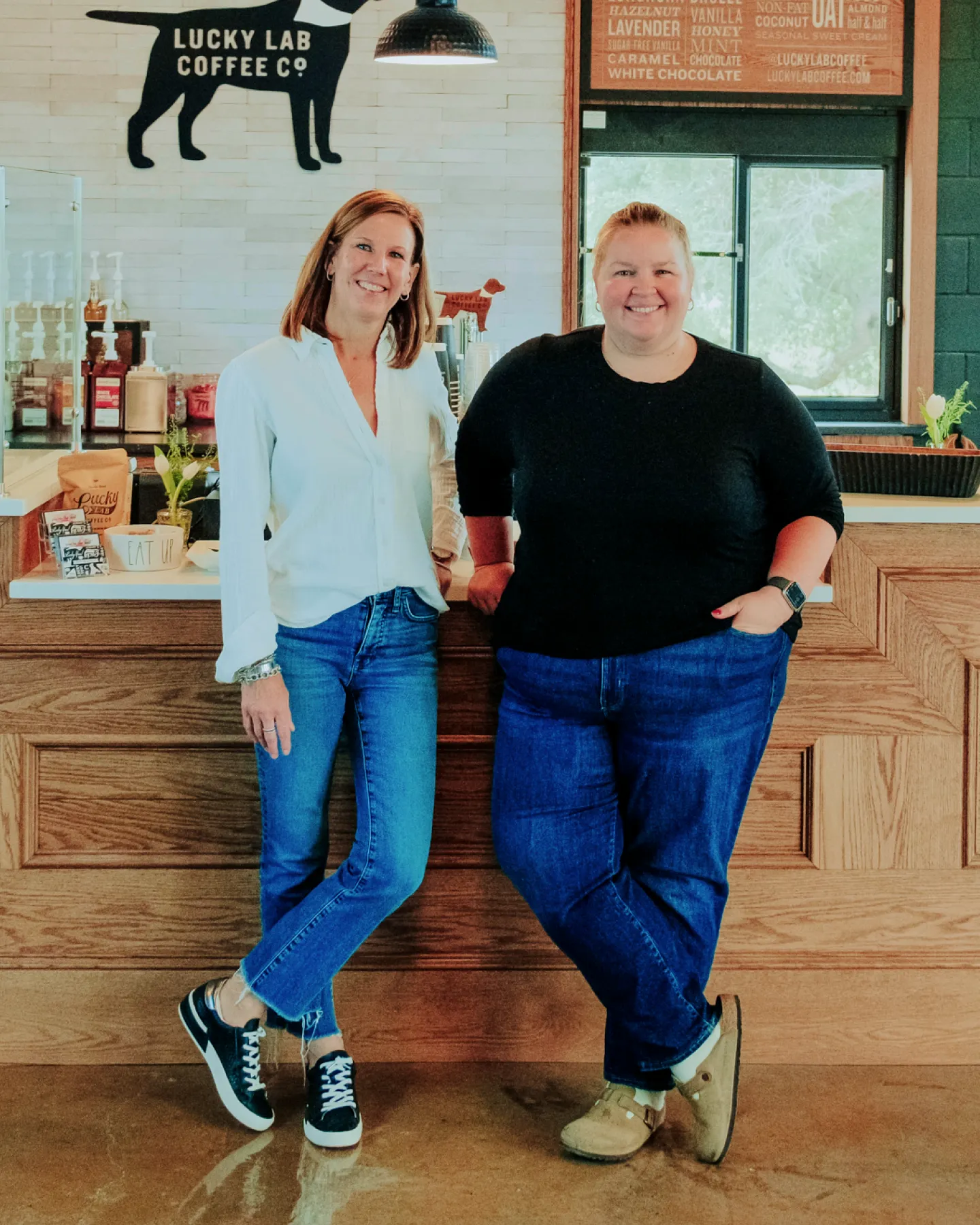 Two smiling women standing in front of a wooden counter with Lucky Lab Coffee Co. logo behind them.