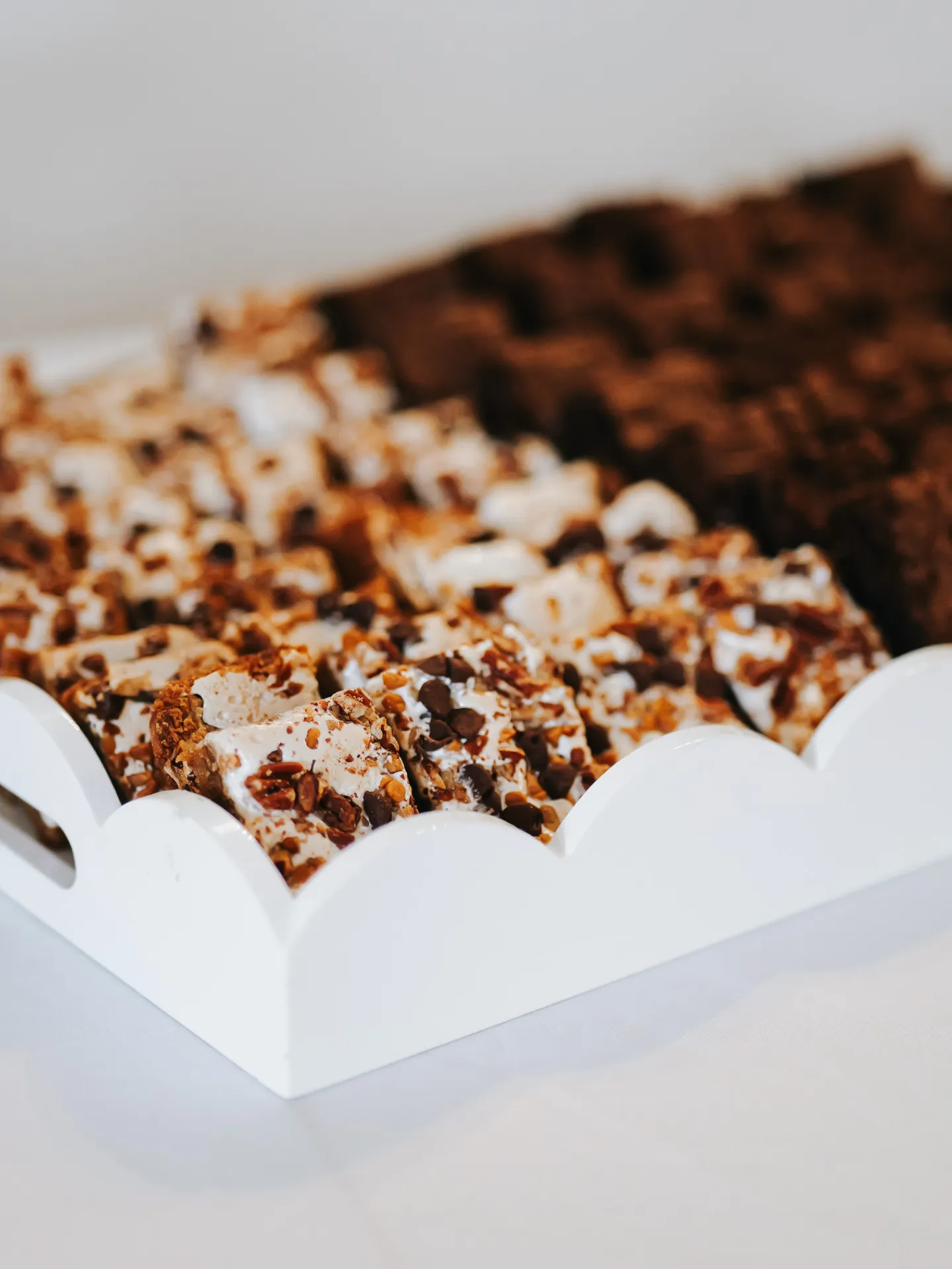 Close-up of white tray holding rows of chocolate chip and nut dessert bars and dark brownies.