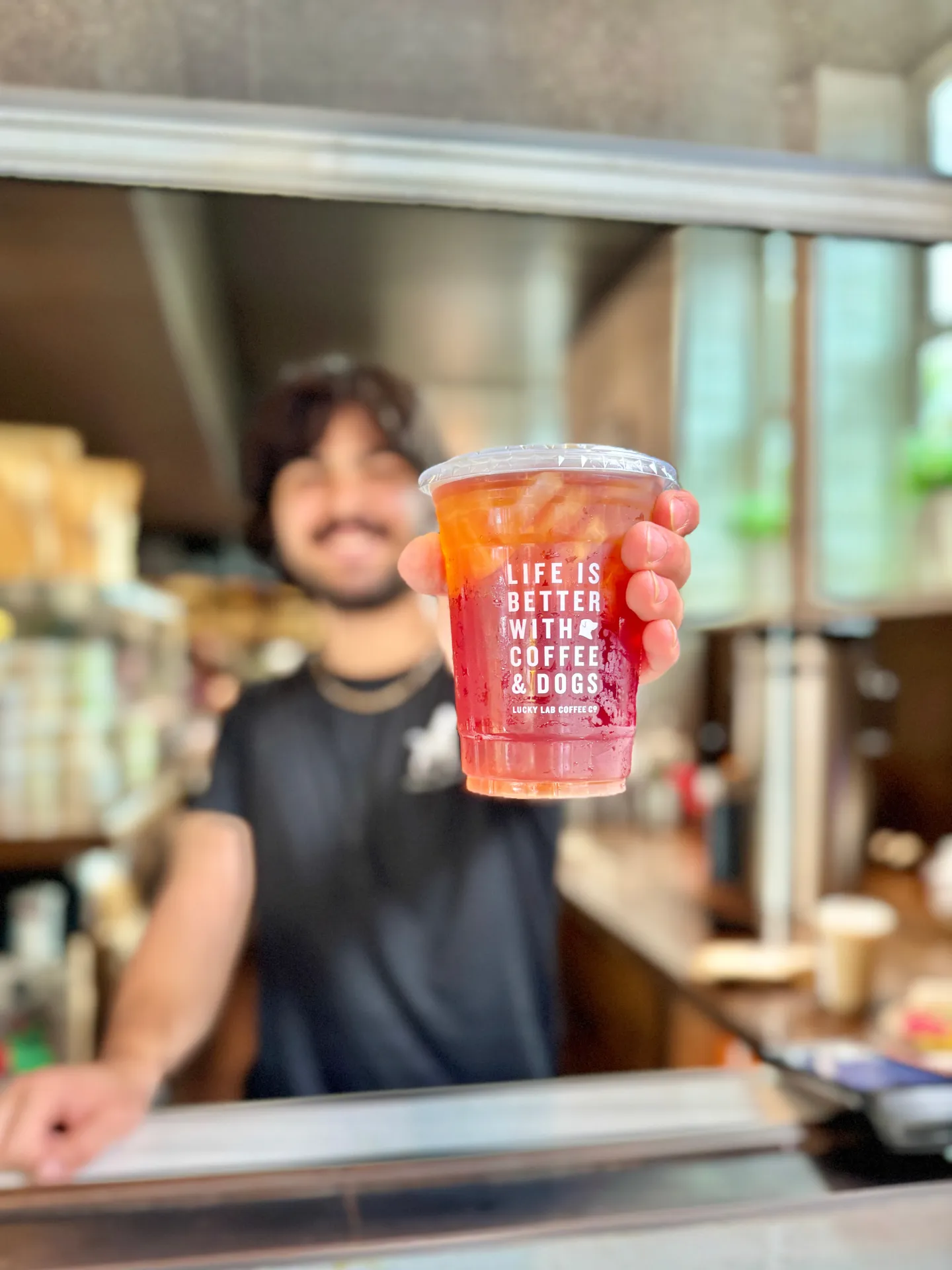 Person holding iced coffee cup with text: Life is better with coffee & dogs in a cafe.
