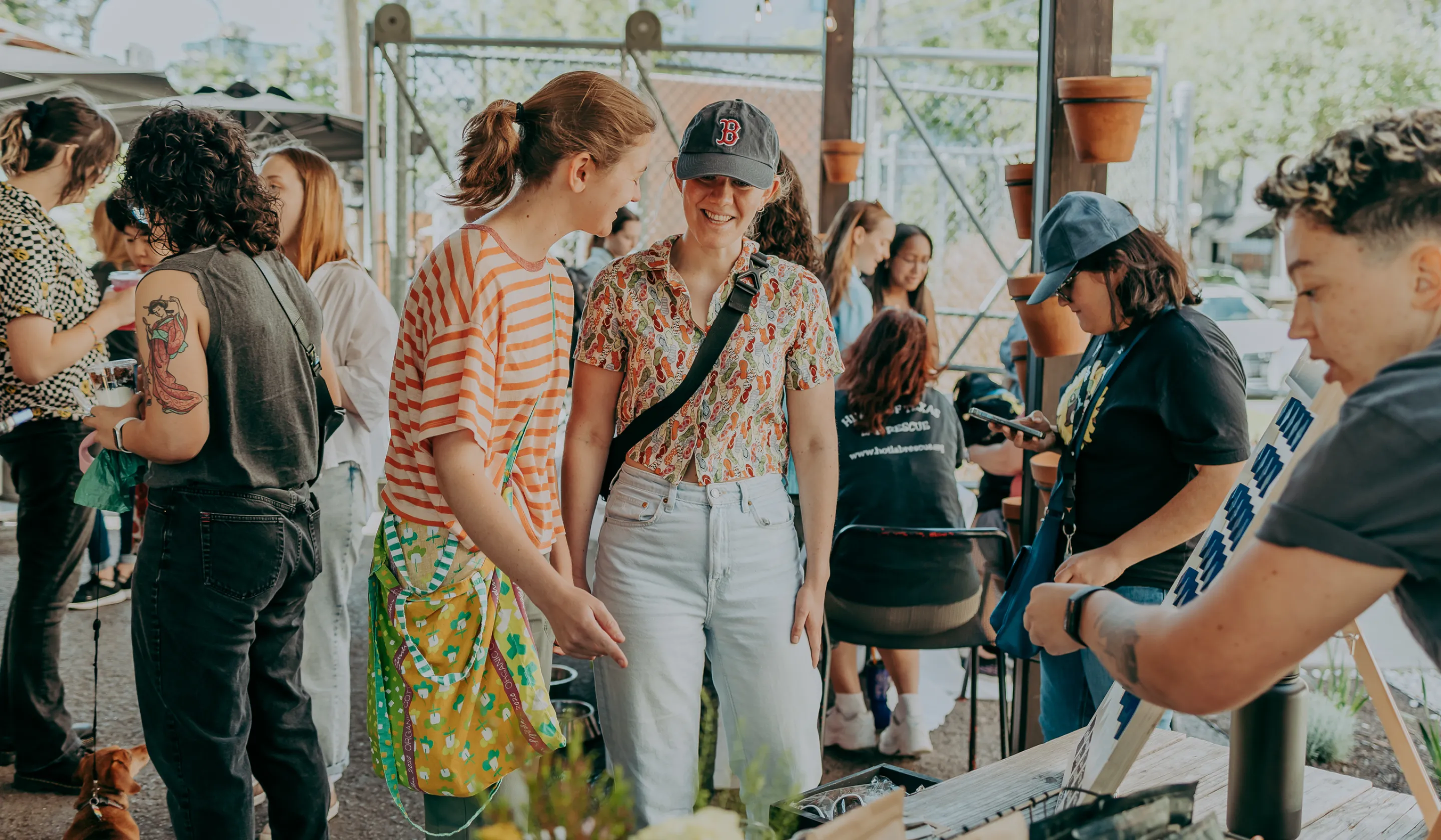Group of people socializing outdoors at a casual gathering with potted plants and a dog.