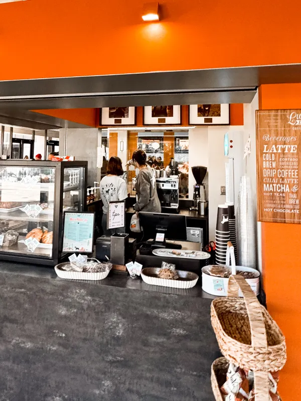 Coffee shop counter with baked goods on display and two people at the espresso machine.