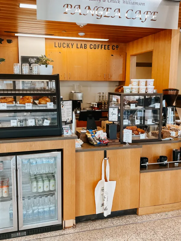 Interior view of Pangea Cafe with Lucky Lab Coffee counter, pastry displays, and bottled drinks fridge.