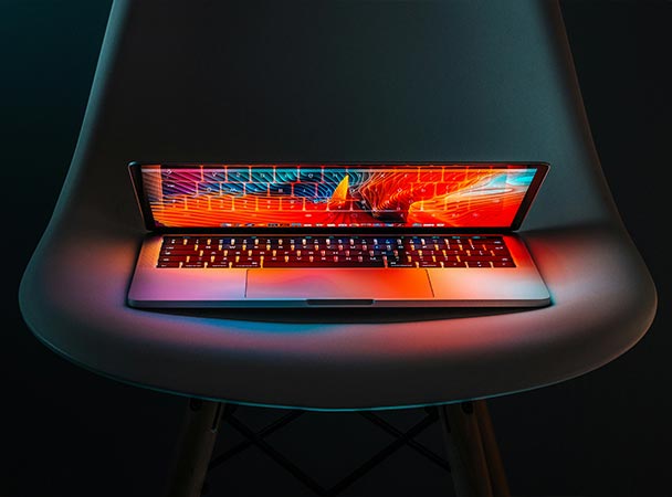 A laptop placed on a modern chair, with a vibrant, colorful display glowing in a minimalist setting.