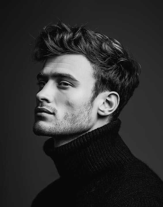 Black and white portrait of a young man in a dark turtleneck sweater, shown in side profile with textured hair and soft studio lighting