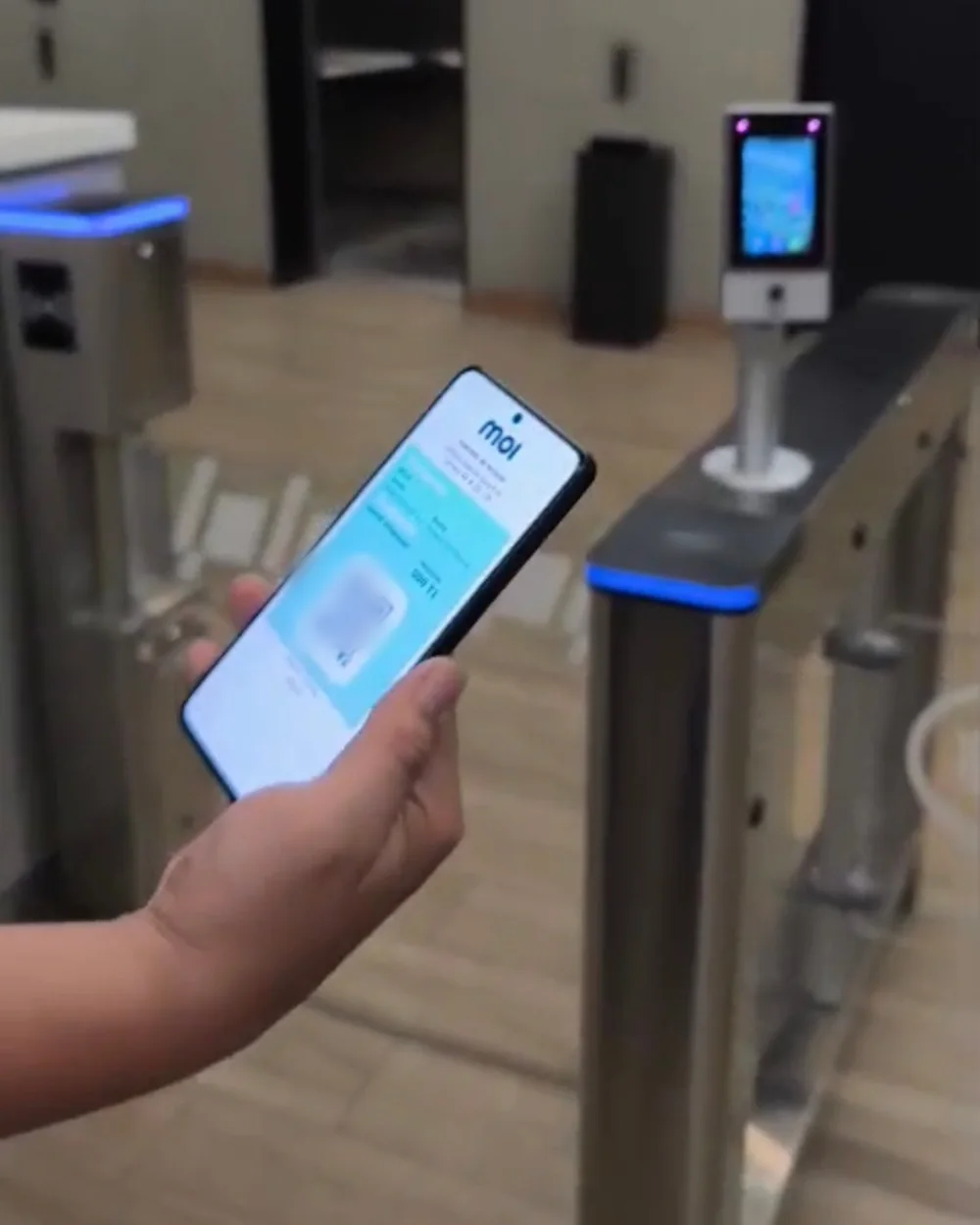 Visitante mostrando su pase QR de la app de MOI frente a un torniquete con lector facial instalado por MOI