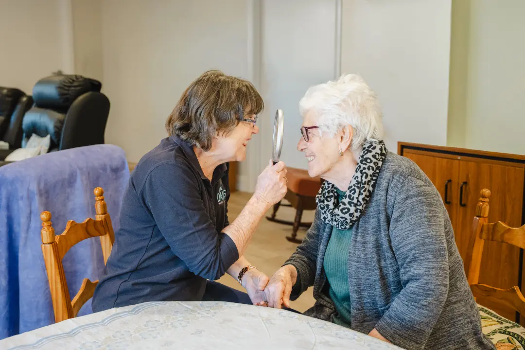 Registered Nurse laughing with aged care client about size of magnifying glass