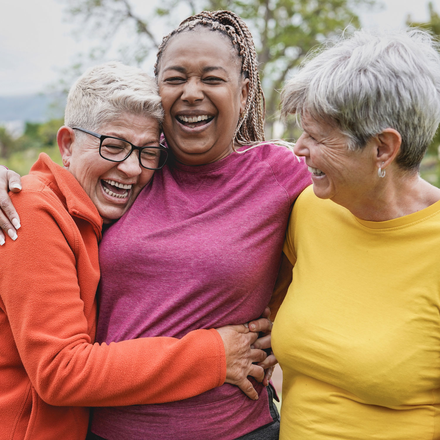 Three women laughing and hugging each other outdoors, showing joy and friendship.