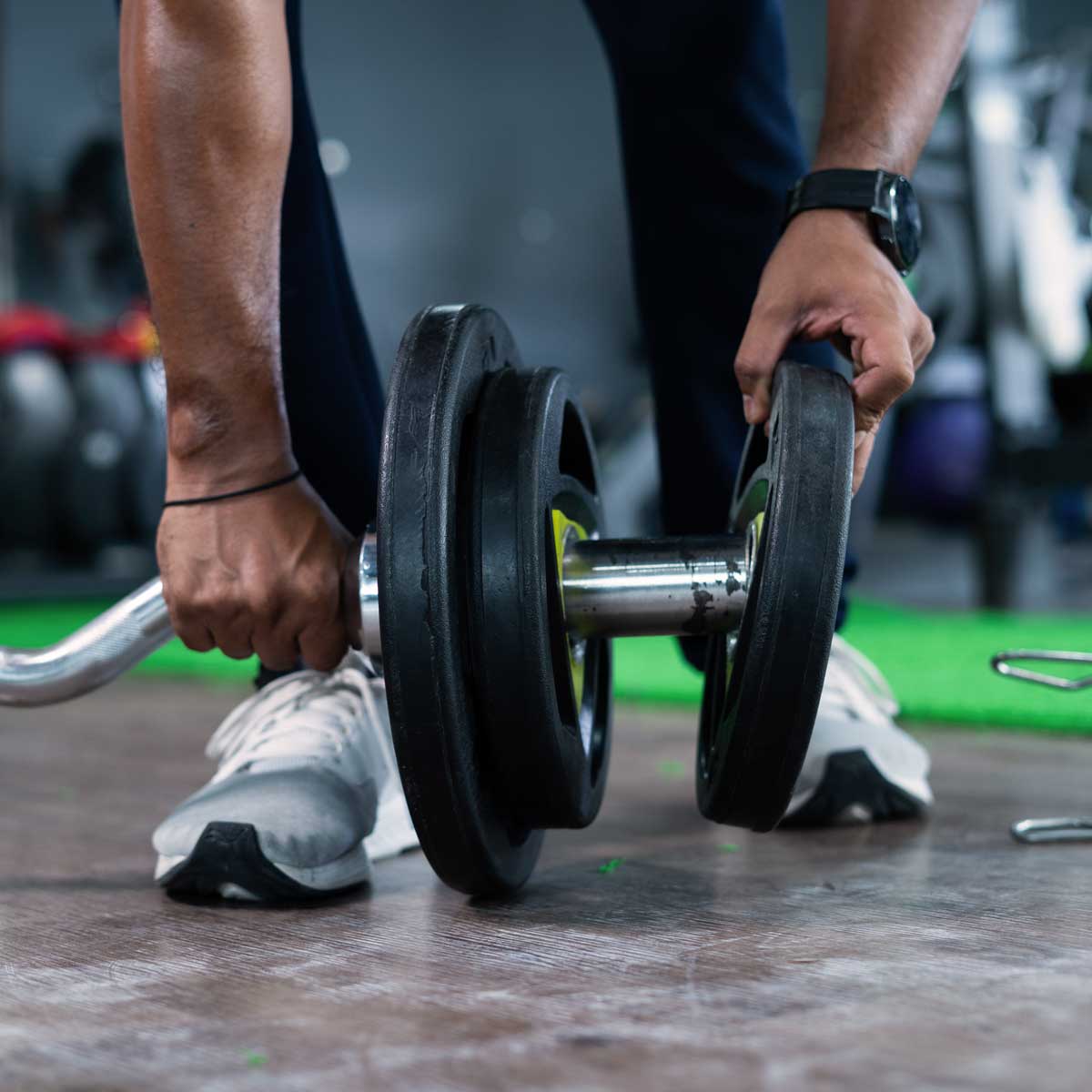 Person gripping a loaded barbell on gym floor, preparing for weightlifting.