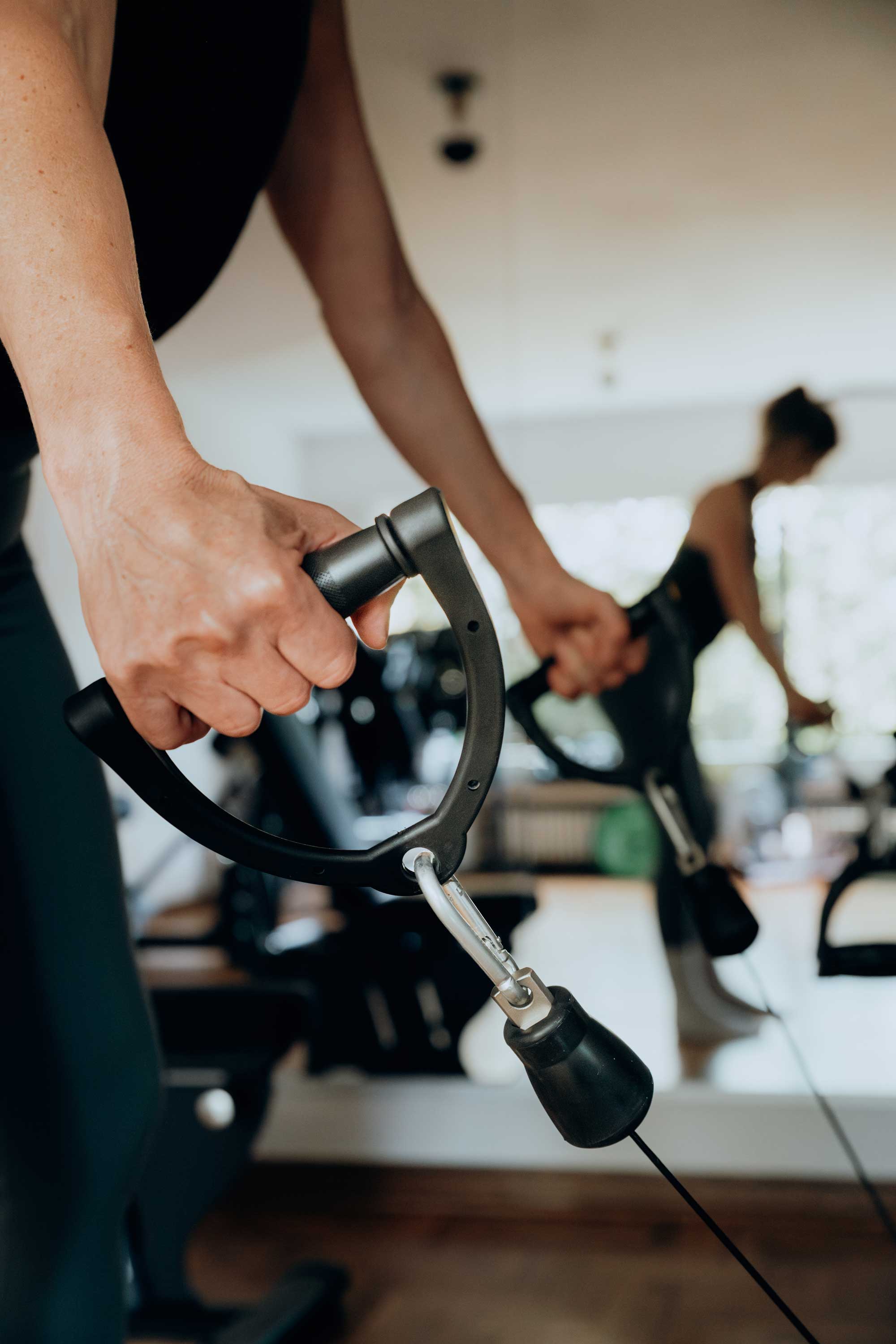 Close-up of a person gripping a cable machine handle at a gym with a blurred reflection in the mirror.