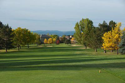 Golf course fairway lined with trees showing autumn colors under a partly cloudy sky.