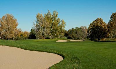 Golf course fairway with a sand bunker in the foreground and trees in the background under a clear blue sky.